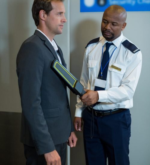 Airport security officer using a hand held metal detector to check a commuter in airport